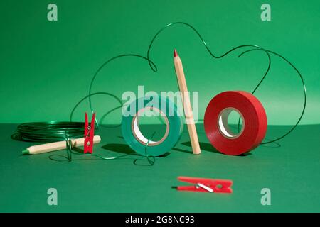Creative art set pencils, red and green tape, pins, green wire on green back Stock Photo