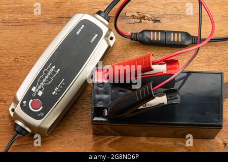 High angle view of battery charger equipment is charging a dry battery on wooden table. Stock Photo