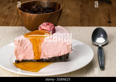 Side view of delicious homemade frozen strawberry cheesecake topping with preserved dried strawberry and honey in white ceramic dish on table mat with Stock Photo