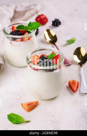 Two portions of greek yogurt with summer berries in glass jars on light stone background. Summer healthy breakfast Stock Photo