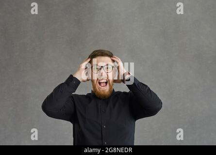 Stressed man touching head and screaming standing over grey studio background Stock Photo