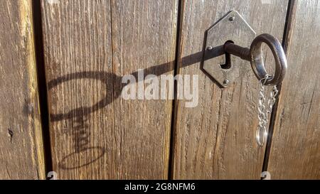 Rural key lock with hanging chain. The key casts a shadow over wooden weathered texture Stock Photo