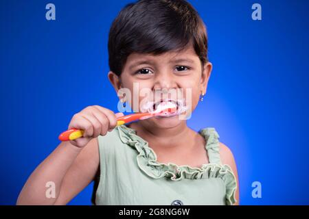 Portrait of girl kid brushing teeth on blue color background - concept of child healthy tooth by cleaning daily Stock Photo