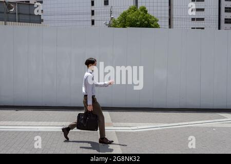 A Japanese salaryman or male office worker, wearing a face mask against COVID19 walks with a briefcase in Shinjuku, Tokyo, Japan. Stock Photo