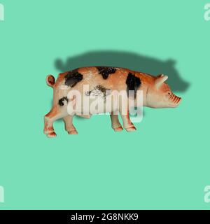 Children's toy figurine of pig on colored background. Old scratched toy isolated against green. Stock Photo