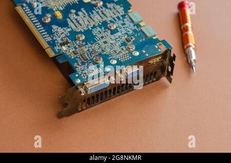 Computer repair services and components concept. Computer graphic card and screwdriver on brown. Close-up, selective focus. Stock Photo