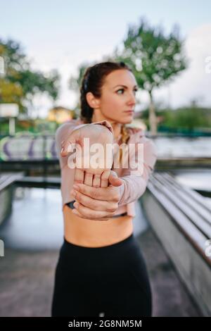 Young sportswoman stretching hands and wrists outdoors. Selective focus on hand in foreground Stock Photo