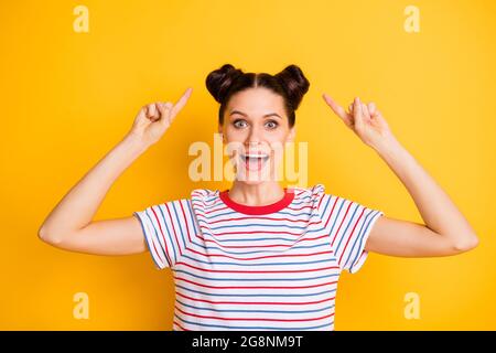 Photo of sweet impressed young woman wear striped t-shirt showing fingers hairdo isolated yellow color background Stock Photo