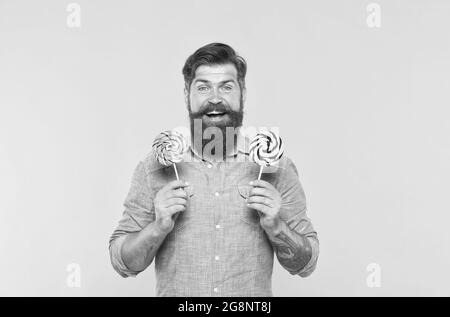 Happy bearded man hold tasty rainbow swirl candy pops great for birthday party and candy buffet yellow background, celebration Stock Photo