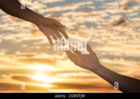 Giving a help hand concept. Reaching hand helping, hope and support each other over sunset background. Stock Photo