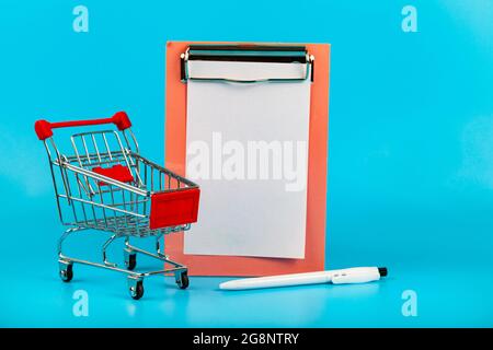 Shopping cart, paper and pen on a blue background. Concept: shopping planning. Stock Photo