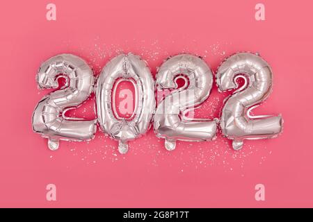 Silver foil balloons numeral 2022 and confetti on pink background Happy New year 2022 celebration Flat lay Stock Photo