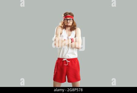 Funny nerd in gym shorts, tank top, headband and glasses pretending to be tough guy Stock Photo