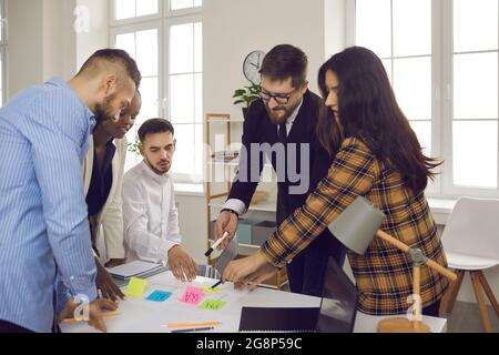 Business team writes notes on colored sticky stickers while discussing a startup project. Stock Photo