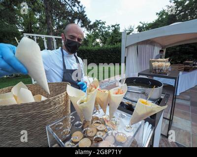 MILANO, ITALY - Jul 07, 2021: A Catering chef wearing a Covid mask and serving seafood in a buffet at a wedding venue Stock Photo