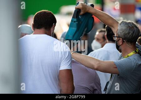 Glasgow, Scotland, UK. 21 July 2021.  PICTURED: A crew member (right) uses a leaf blower to blow cold air down the back of Olivier Richters’ (AKA The Dutch Giant, seen sitting down in the light purple shirt with his back to camera) back to dry the sweat patch on the back of his shirt, then pats him on the back before the next film. take. Filming on the set of Indiana Jones 5 in the middle of Glasgow city centre as the Hollywood blockbuster sets up Glasgow as New York City. Credit: Colin Fisher Stock Photo