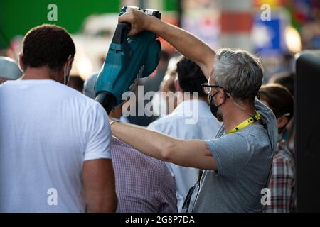 Glasgow, Scotland, UK. 21 July 2021.  PICTURED: A crew member (right) uses a leaf blower to blow cold air down the back of Olivier Richters’ (AKA The Dutch Giant, seen sitting down in the light purple shirt with his back to camera) back to dry the sweat patch on the back of his shirt, then pats him on the back before the next film. take. Filming on the set of Indiana Jones 5 in the middle of Glasgow city centre as the Hollywood blockbuster sets up Glasgow as New York City. Credit: Colin Fisher Stock Photo