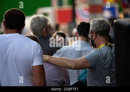 Glasgow, Scotland, UK. 21 July 2021.  PICTURED: A crew member (right) uses a leaf blower to blow cold air down the back of Olivier Richters’ (AKA The Dutch Giant, seen sitting down in the light purple shirt with his back to camera) back to dry the sweat patch on the back of his shirt, then pats him on the back before the next film. take. Filming on the set of Indiana Jones 5 in the middle of Glasgow city centre as the Hollywood blockbuster sets up Glasgow as New York City. Credit: Colin Fisher Stock Photo