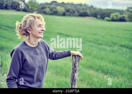 Portrait of a young mature caucasian woman standing outdoor leaning on a path pole in spring time. Navarre, Spain, Europe. Stock Photo