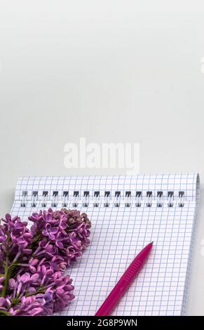 Notebook lilacs on white background. Spiral notebook and pen. Notepad with pen and flowers. Stock Photo