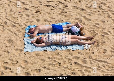 Bournemouth, Dorset UK. 22nd July 2021. UK weather: another hot, sunny and humid day at Bournemouth beaches as the heatwave continues and sunseekers head to the seaside to enjoy the sunshine.  Young couple sunbathing on beach - sunbather sunbathers. Credit: Carolyn Jenkins/Alamy Live News Stock Photo