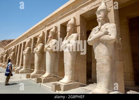 A tourist admires the row of Osiris pillars which stand along the upper terrace at the Mortuary Temple of Hatshepsut at Stock Photo
