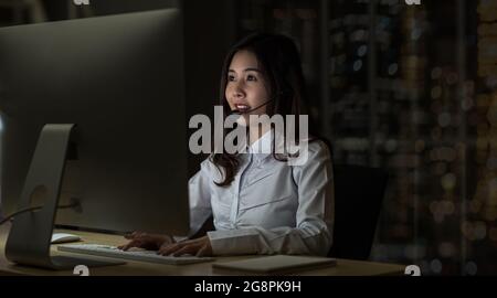 Asian Woman support desk working hard late in night shift at office, Call center and customer service concept Stock Photo