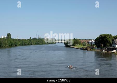 seen from chiswick bridge, two female rowers on a wide stretch of the river thames with kew rail bridge in the middle distance Stock Photo