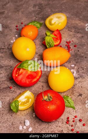 Culinary background with ripe tomatoes and basil leaves. Various colorful vegetables, sea salt, and pink peppercorn on a dark stone concrete backgroun Stock Photo