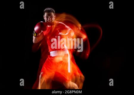 Front view of one professional male boxer in motion, action on black studio background in mixed lights. Stock Photo