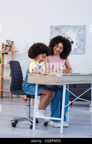 Young african american mother helping daughter with schoolwork at home