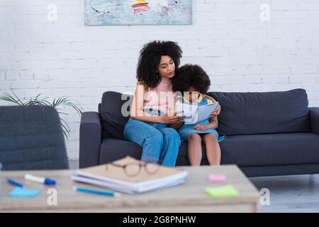 African american mother holding notebook near daughter on couch Stock Photo