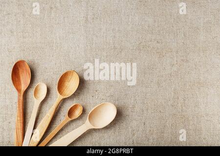 Craft spoons made from different types of wood lie in a row on a hemp burlap fabric Stock Photo