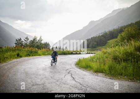 Man riding bicycle on the serpentine mountain road at overcast rainy sky Stock Photo