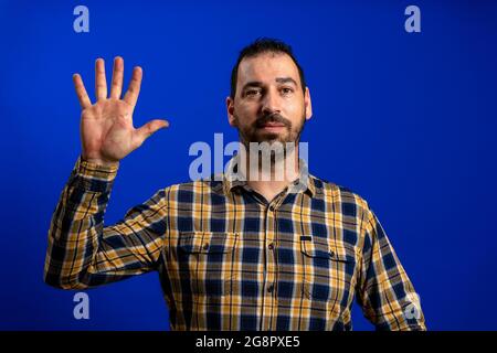 Young handsome caucasian man isolated on blue background saluting with hand with happy expression Stock Photo