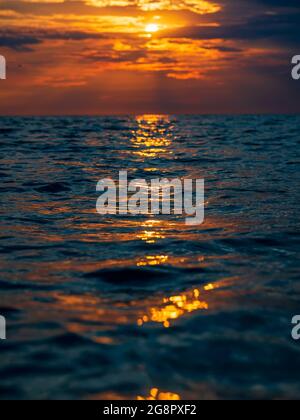 Sunset with clouds, warm colors and waves in ocean. Stock Photo