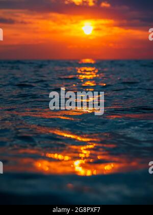 Sunset with clouds, warm colors and waves in ocean. Stock Photo