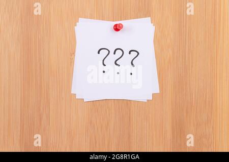 White Sticky Notes with Three Question Marks Pinned to the Wooden Message Board. To Do List Reminder in the Office. Memo Note at Work Stock Photo