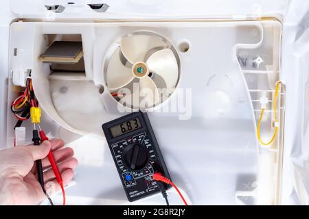 A technician checks an electrician with a digital multimeter in refrigerator fridge. Inside refrigerator repair. Disassembled refrigerator. Removed ba Stock Photo