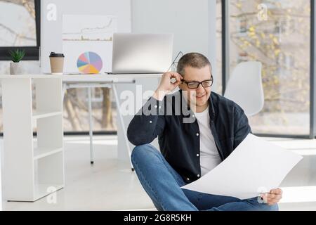 A man dressed in casual style works in the office and looking through business papers. The man works in a remote place of work Stock Photo