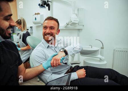 Caucasian male patient sitting in doctors office shaking hands with male nurse after successful checkup Stock Photo