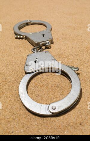 Closed silver handcuffs on the sand, close-up Stock Photo