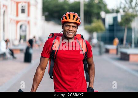 African american delivery man wearing safety helmet smiling and looking at camera in the street. Stock Photo