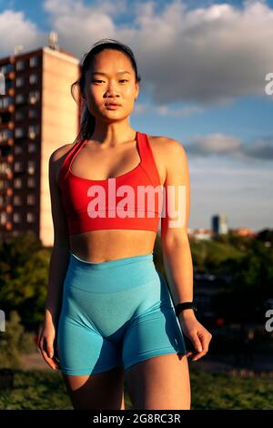 Young chinese woman wearing sports clothes looking at camera and posing in the park during sunset hour. Stock Photo