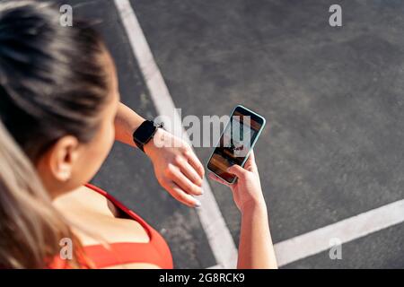 Unrecognized active woman with sports clothes using her mobile phone and looking her smart-watch outdoors. Stock Photo