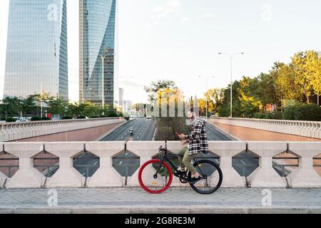 Happy hipster man standing in his bike and using his mobile phone. He is in the city. Stock Photo