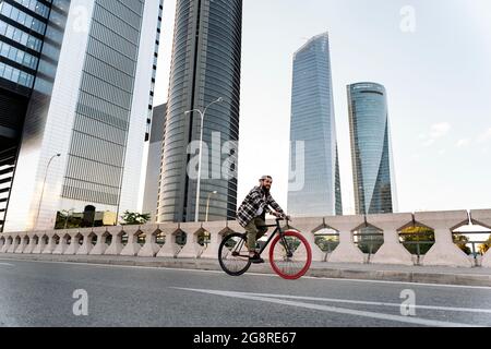 Happy bearded man with long hair smiling and riding his bike in the city. Stock Photo