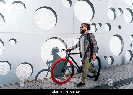 Confident man with long beard walking in the street with his cool bike. Stock Photo