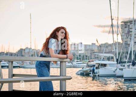 Young redhead woman looks to the sea in a seaport of a city Stock Photo