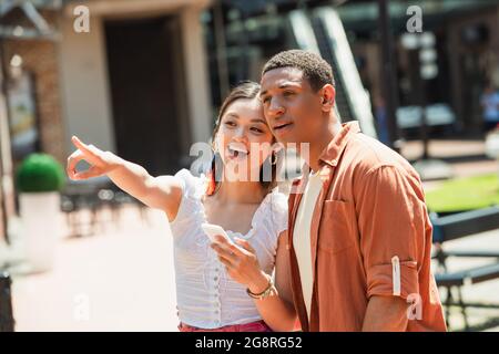 amazed asian woman with smartphone pointing with finger near african american man Stock Photo